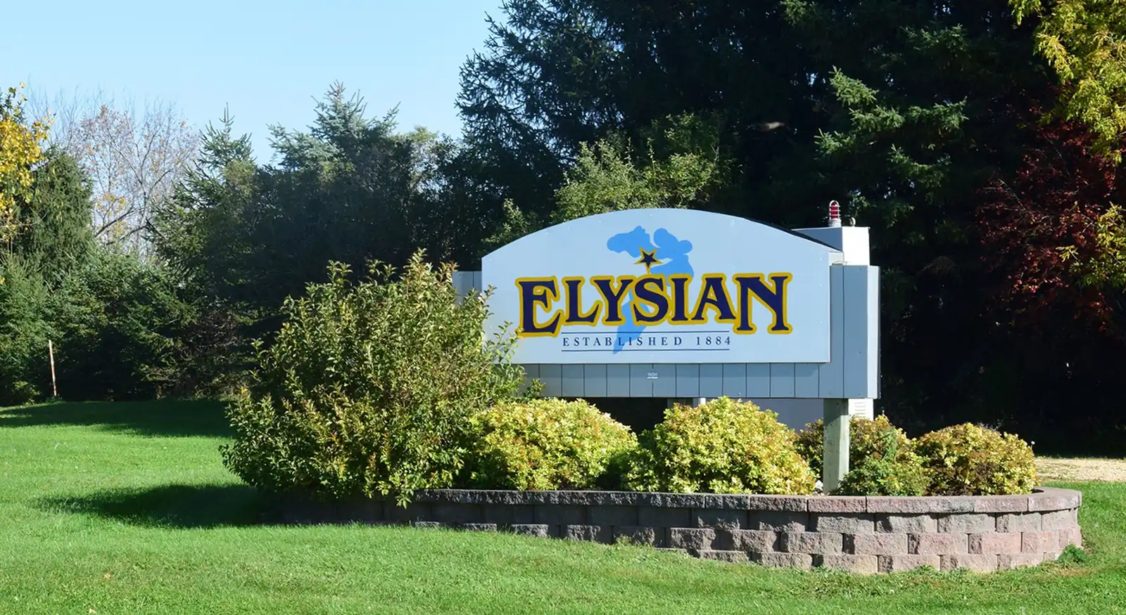 Elysian welcome sign surrounded by flowers and trees